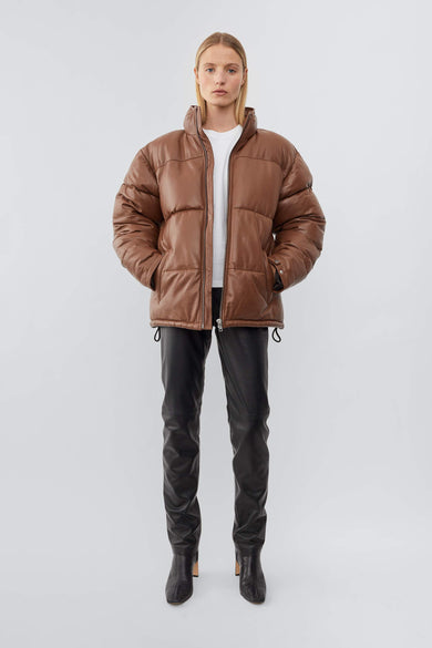 Model wearing down-free, Deadwood leather puffer jacket with zipper closure at center front and waist pockets. Features an inside pocket and drawstring at hem. Here in a cognac brown. Made from recycled leather.
