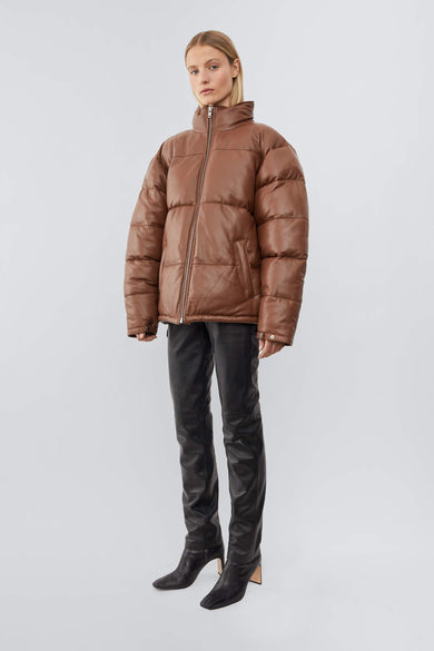 Model wearing down-free, Deadwood leather puffer jacket with zipper closure at center front and waist pockets. Features an inside pocket and drawstring at hem. Here in a cognac brown. Made from recycled leather.