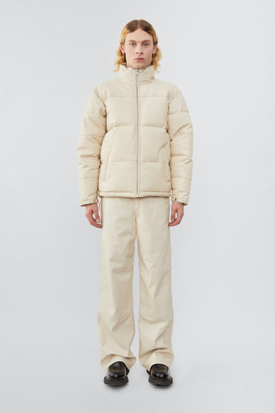 Model wearing down-free, Deadwood leather puffer jacket with zipper closure at center front and waist pockets. Features an inside pocket and drawstring at hem. Here in off-white. Made from recycled leather.