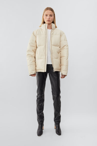 Model wearing down-free, Deadwood leather puffer jacket with zipper closure at center front and waist pockets. Features an inside pocket and drawstring at hem. Here in off-white. Made from recycled leather.