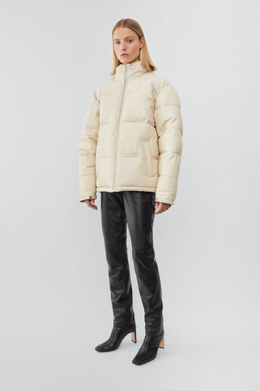Model wearing down-free, Deadwood leather puffer jacket with zipper closure at center front and waist pockets. Features an inside pocket and drawstring at hem. Here in off-white. Made from recycled leather.
