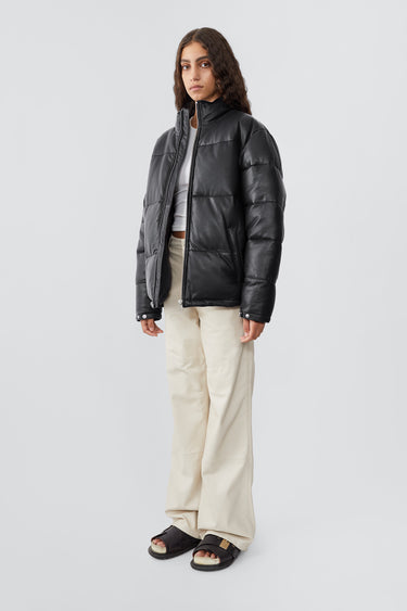 Model wearing down-free, Deadwood leather puffer jacket with zipper closure at center front and waist pockets. Features an inside pocket and drawstring at hem. Made from recycled leather.