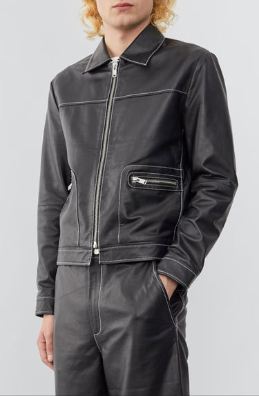 Model wearing  a straight-cut leather Deadwood jacket that echoes both 60's and 90's aesthetics. Black with white stitching all around. Made from upcycled leather.