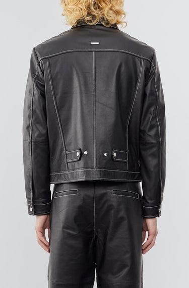 Model wearing  a straight-cut leather Deadwood jacket that echoes both 60's and 90's aesthetics. Black with white stitching all around. Made from upcycled leather.