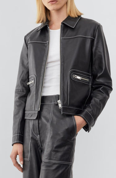 Model wearing a straight-cut leather Deadwood jacket that echoes both 60's and 90's aesthetics. Black with white stitching all around. Made from upcycled leather.