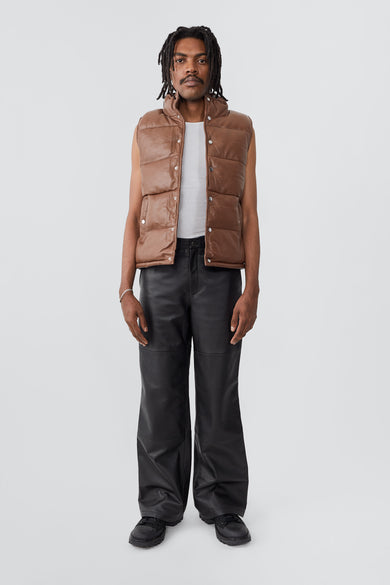 Model wearing Deadwood brown down-free recycled leather puffer vest with push button closure at center front. Waist pockets and a drawstring at the hem. 
