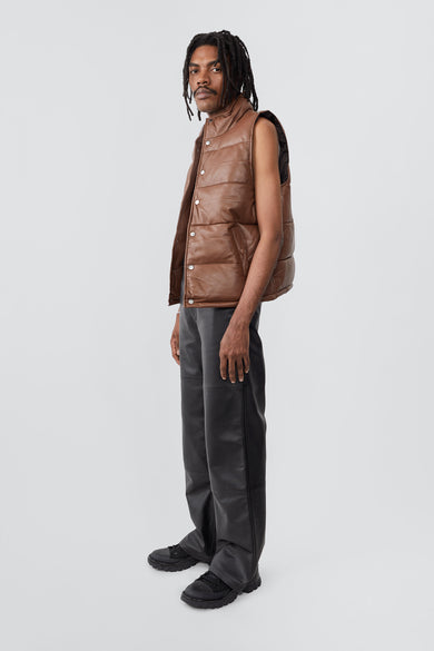 Deadwood brown down-free recycled leather puffer vest with push button closure at center front. Waist pockets and a drawstring at the hem. 