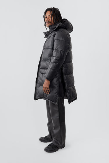 Model wearing down-free, black Deadwood leather puffer parka made from recycled lambskin leather. Zipper closure at center-front, side vent zippers, duo front pockets, and pockets at waist.